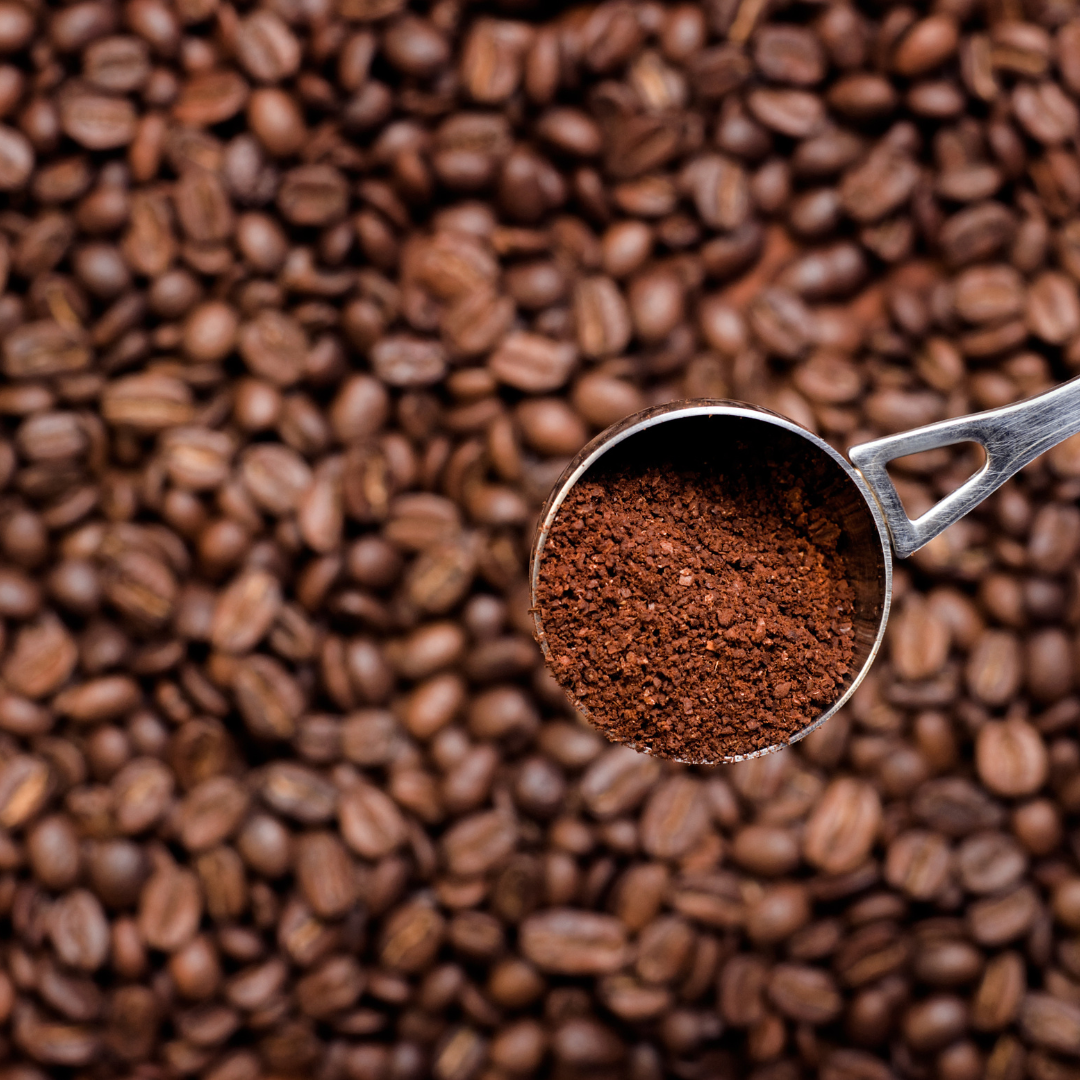 Metal scoop filled with ground coffee on a background of coffee beans