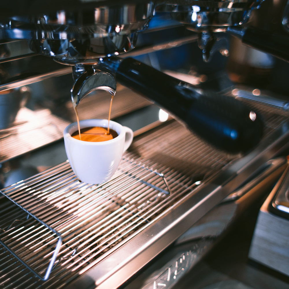 Commercial coffee machines pouring espresso into a white coffee cup